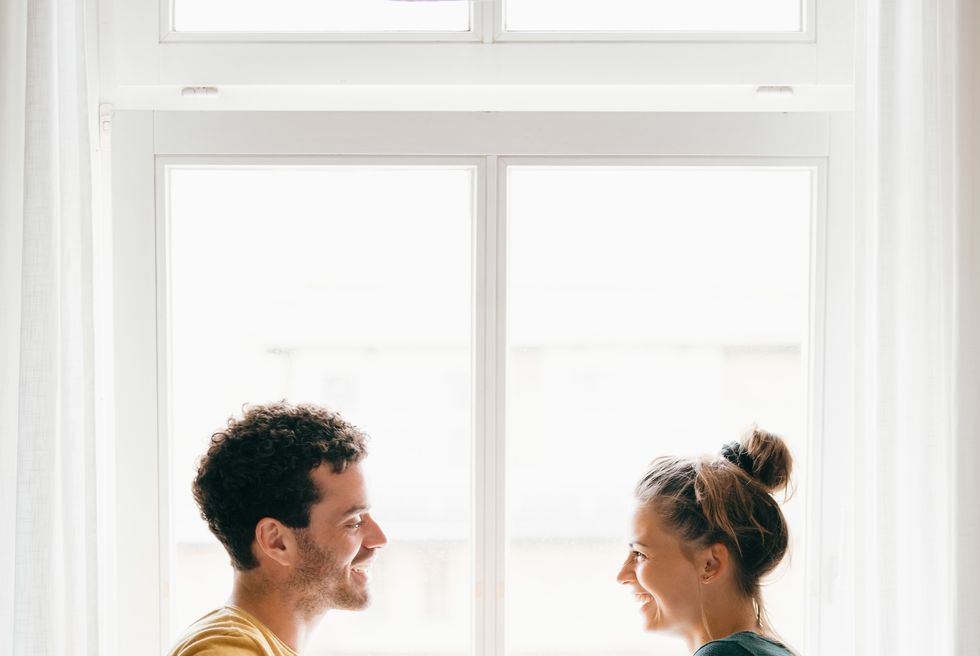 side view of happy couple talking while standing by window at home