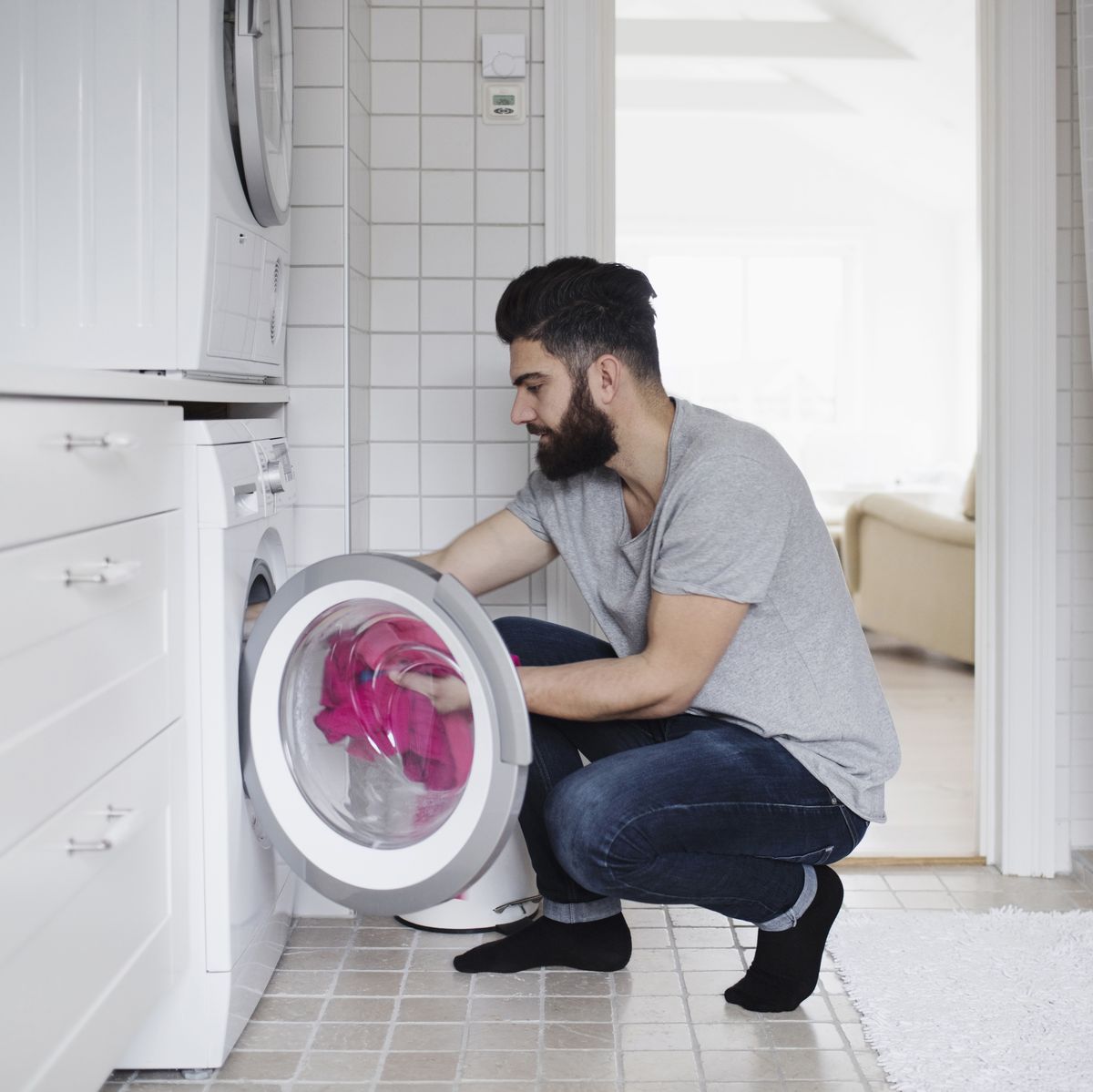 Side view of man crouching while loading clothes in washing machine at home