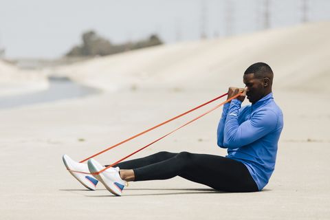 side view of man stretching resistance band while sitting on land during sunny day