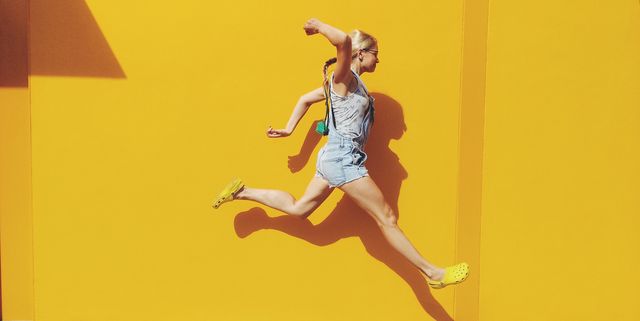 Side View Of Mid Adult Woman Jumping On Footpath Against Yellow Wall