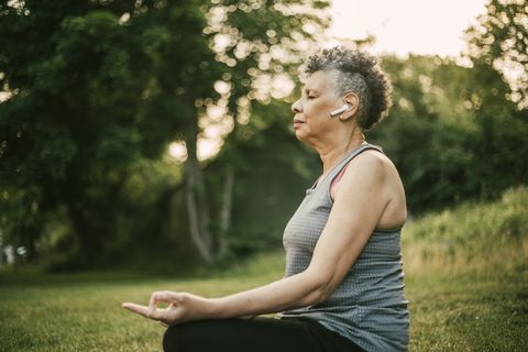 side view of senior woman with in ear headphones sitting in lotus position at park