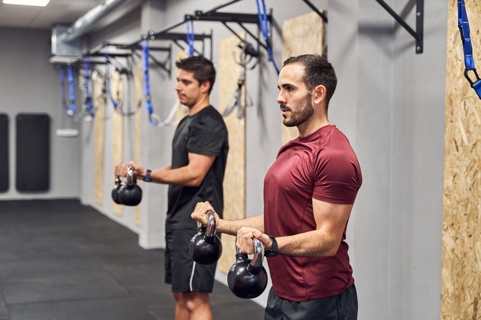 side view of two athletes training biceps with kettlebells during a functional workout class at the gym