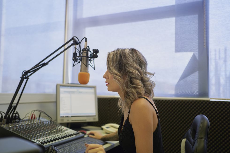 side view of unrecognizable female presenter with blonde hair sitting in radio studio in front of microphone during her radio show