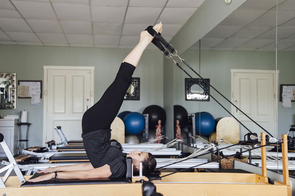 side view of woman in gym using pilates reformer
