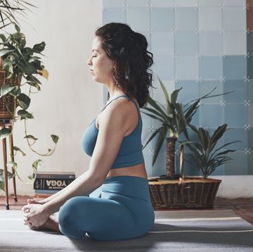 side view of woman meditating while sitting by potted plants at home
