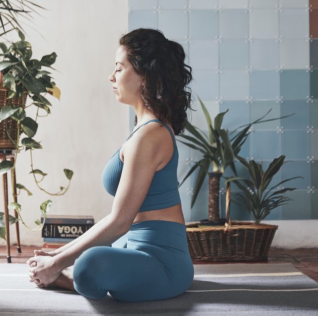 side view of woman meditating while sitting by potted plants at home