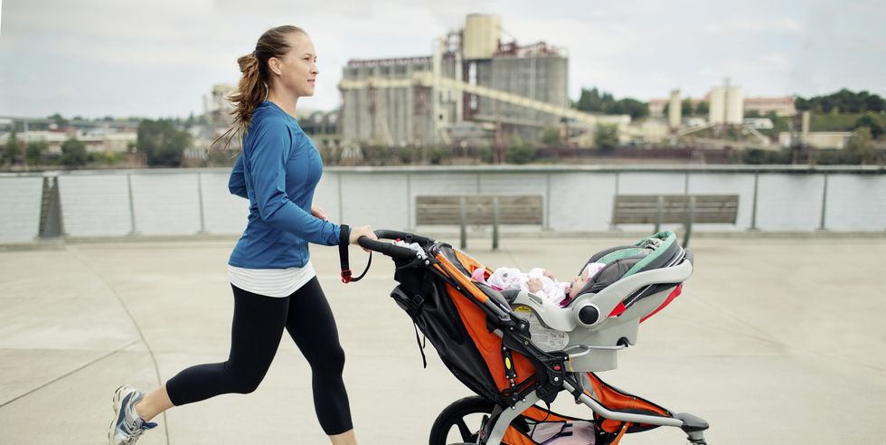side view of woman pushing baby stroller while jogging in city