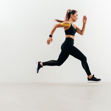 side view of woman running against a white wall jogger with kinesiology tape on her shoulder sprinting