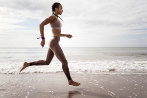 side view of young female runner running barefoot along waters edge at beach