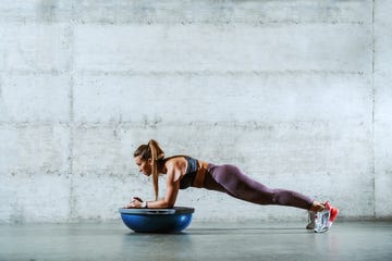 Side view of young muscular caucasian sporty brunette in sportswear with ponytail doing planks and leaning on bosu ball. Healthy lifestyle concept.