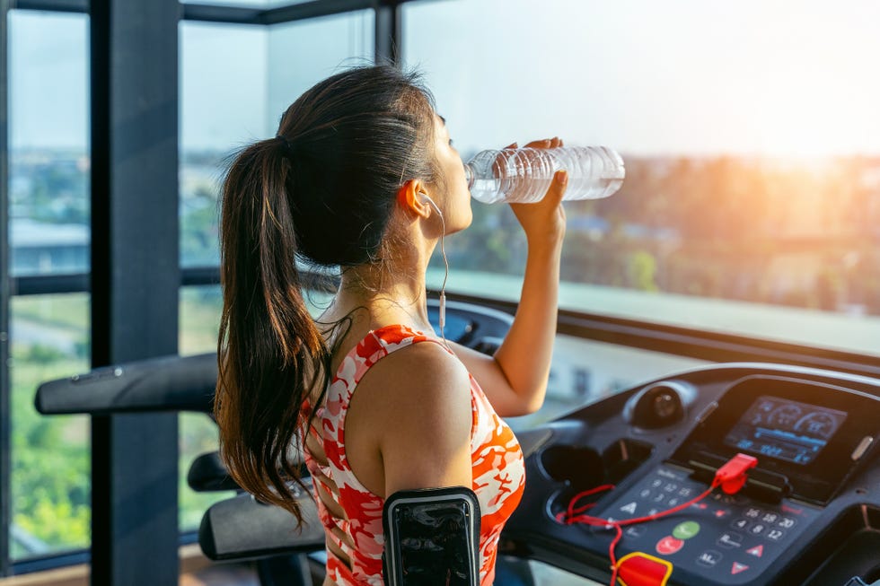 Side View Of Young Woman Drinking Water While Exercising At Gym