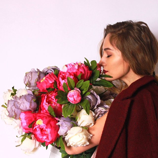 side view of young woman smelling bouquet against white background
