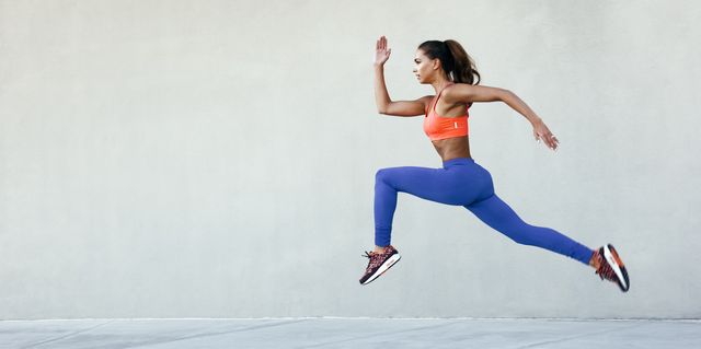 Side view of young woman wearing sports clothing in mid air striding stance