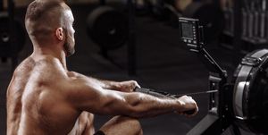 side view photo of shirtles man using th rowing machine while training