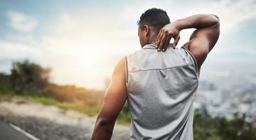 rearview shot of a sporty young man touching his neck while exercising outdoors