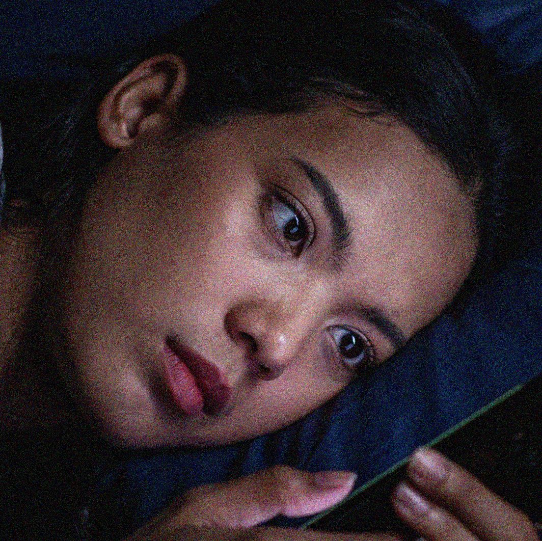 a young asian woman in bed in the dark looking at her phone