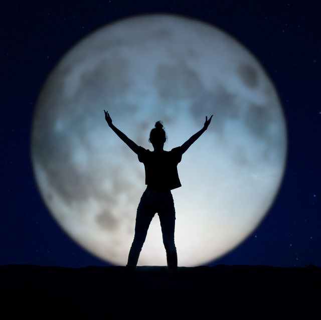 silhouette of a woman standing in the night with the arms up, giant moon in the background