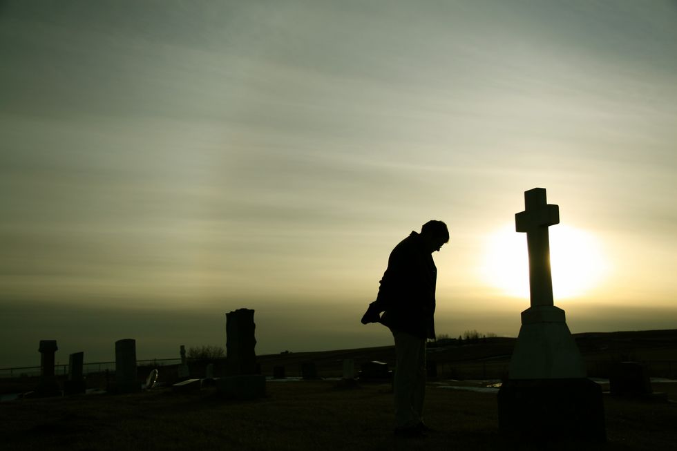 silhouette of caucasian man mourning at graveyard