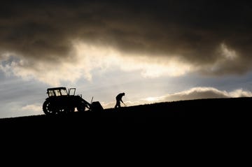 silhouette of farmer working and tractor up high in the clouds