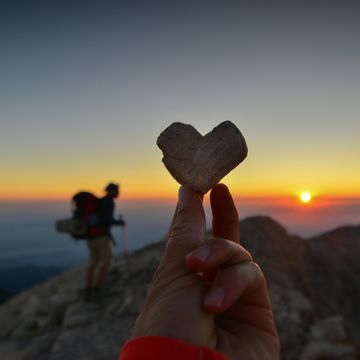 silhouette of man with backpack and heart shaped stone in a mountain at sunset