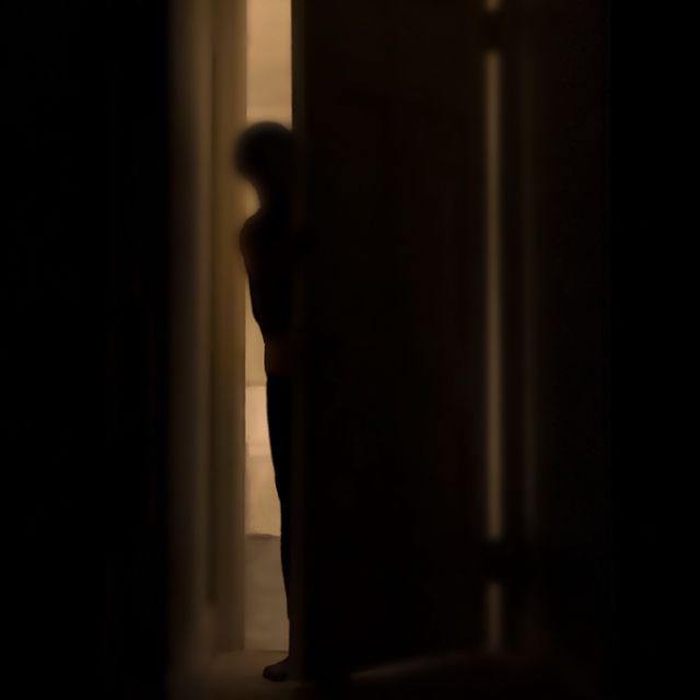silhouette of person peeking into dark room through a cracked door