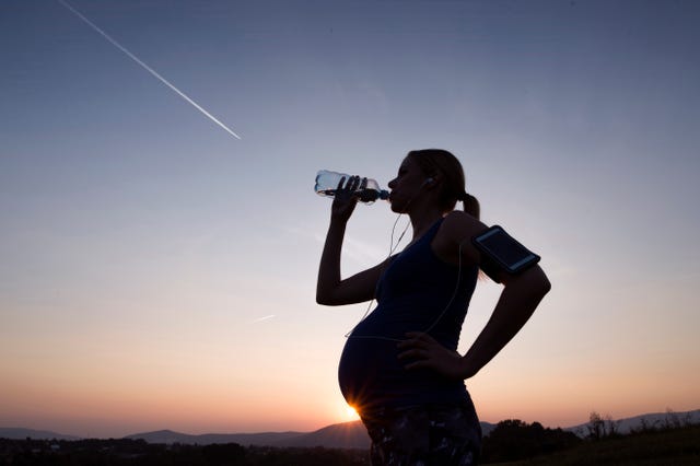 silhouette of pregnant woman drinking water from bottle at sunset