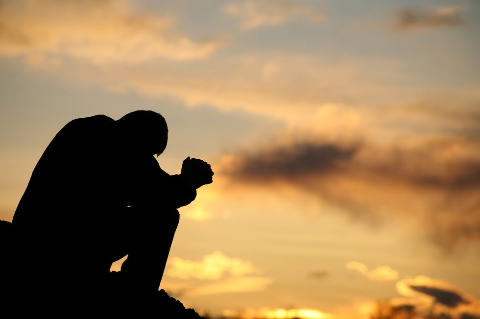 silhouette of unrecognizable man praying outside