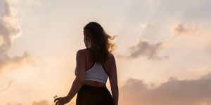 silhouette of young woman in the sport clothes with bottle of clear mineral water on the sunset sky backgrounds the concept of healthy lifestyle