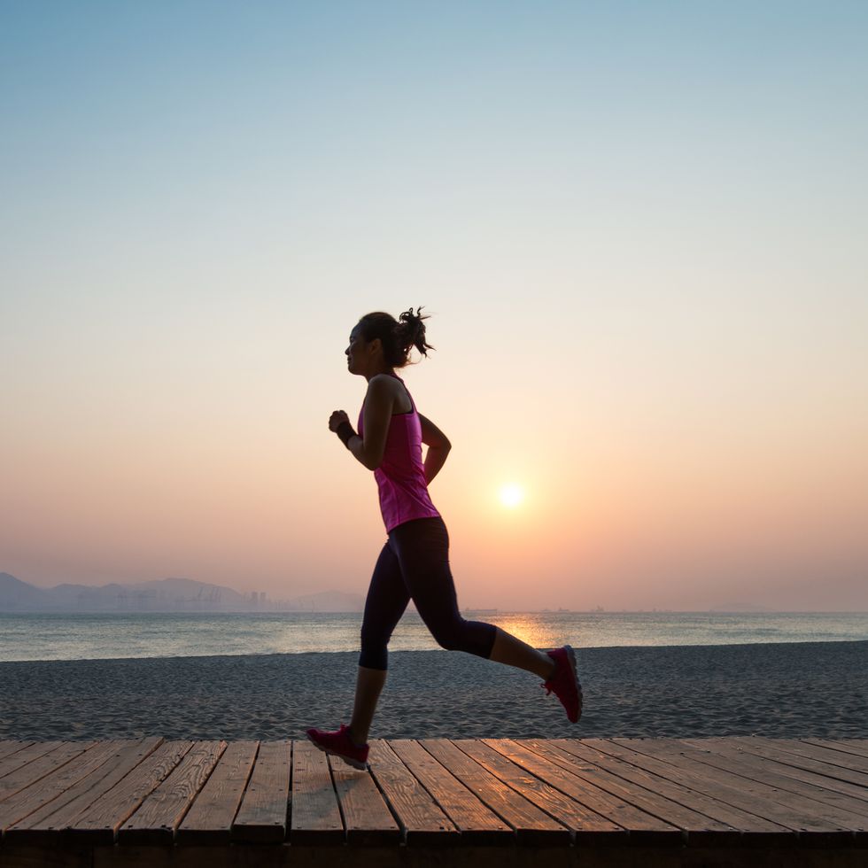 silhouette of young woman jogging on shore at sunrise