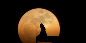 silhouette woman sitting on cliff against moon at night