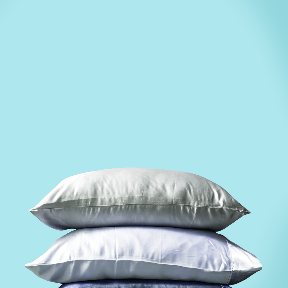 a stack of 3 pillows in gray, white, and blue silk pillowcases on an aqua background