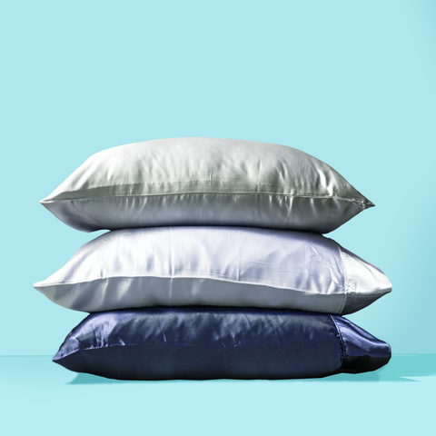 a stack of 3 pillows in gray, white, and blue silk pillowcases on an aqua background