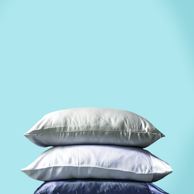 a stack of 3 pillows in gray, white, and blue silk pillowcases on an aqua background