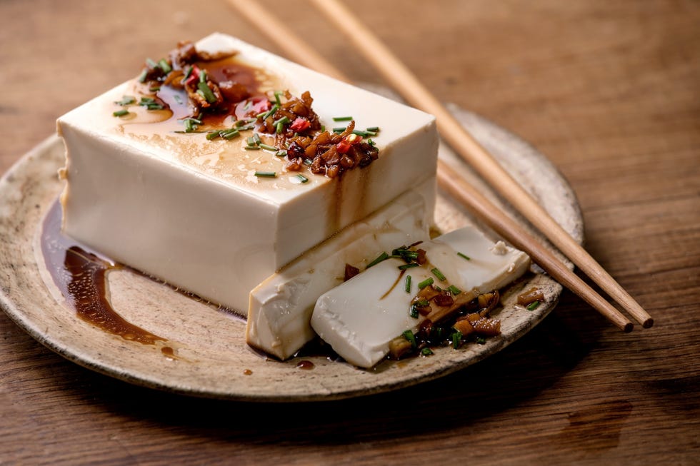 silk tofu japanese soy cheese whole piece with chili chive ginger and soy sauce topping on ceramic plate with chopsticks over wooden table