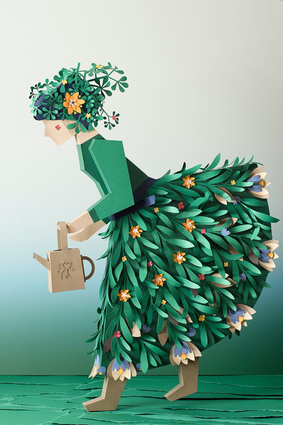 mujer jardinera hecha de papel con regadera y falda de hojas verdes