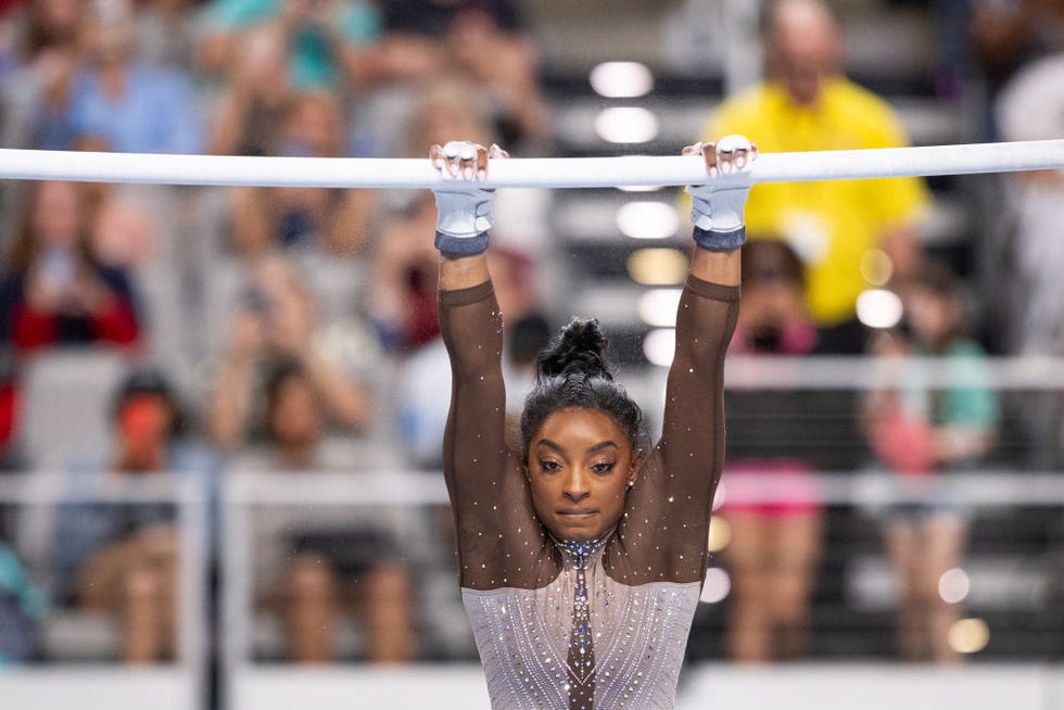 simone biles hanging from the uneven bars during a gymnastics routine