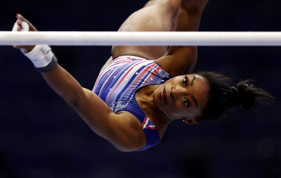 gymnast simone biles upside down in the air as she looks toward one of the uneven bars