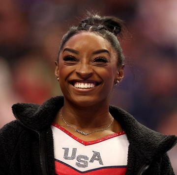 simone biles smiling while wearing a usa uniform at a gymnastics meet