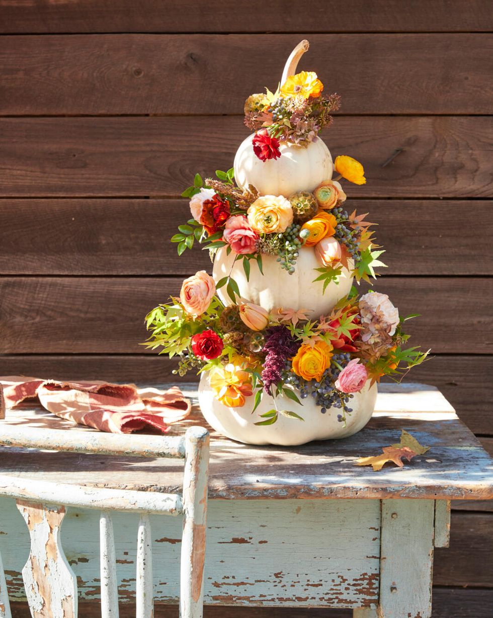 three white pumpkins stacked up with flowers and berries in the crevices
