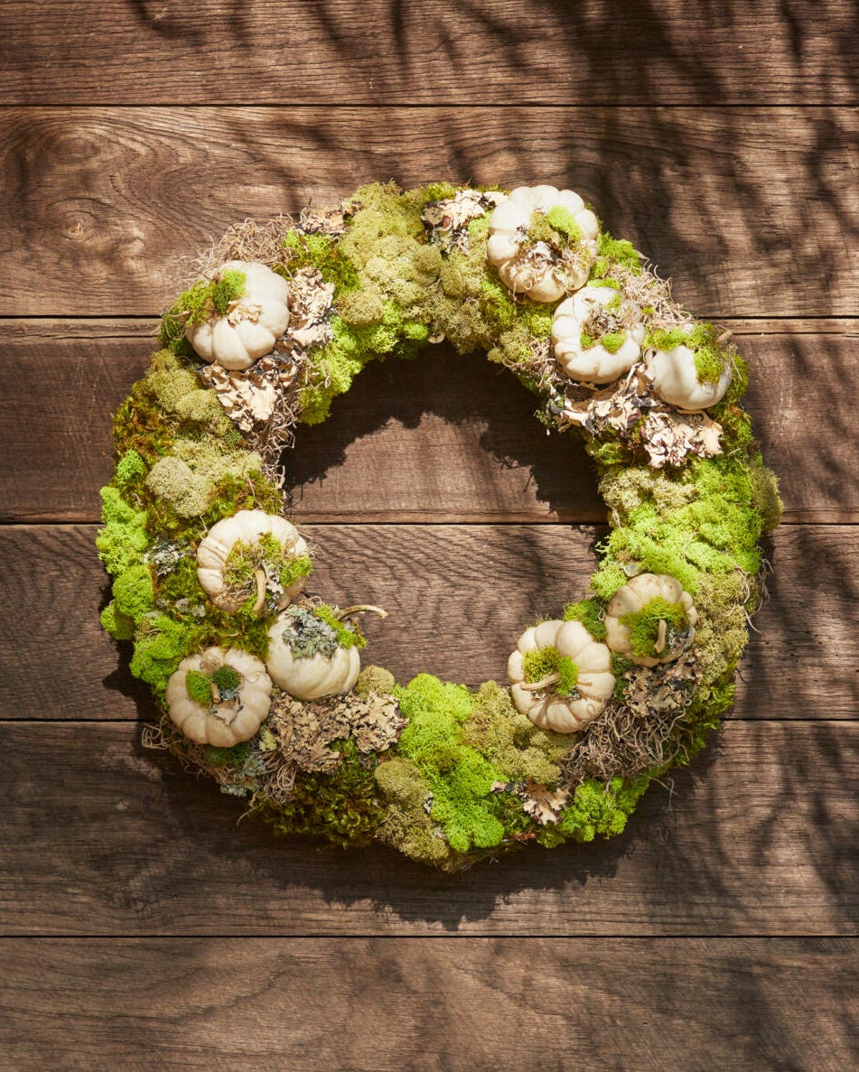 a wreath made from moss lichen and small white pumpkins hung on a brown barn