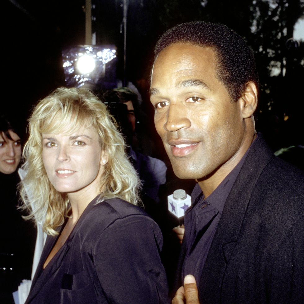 nicole brown simpson smiles at the camera and stands next to oj simpson who smiles and looks to the left