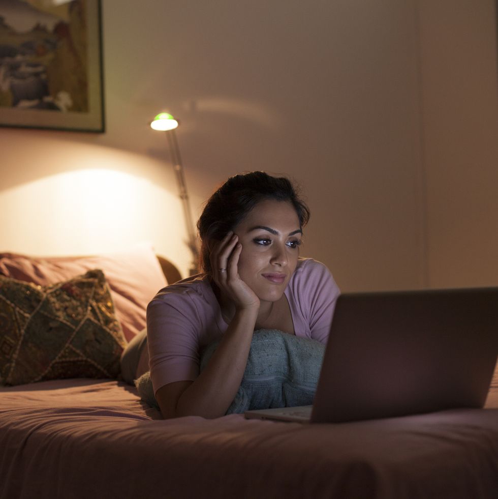 Singapore, Young woman relaxing with laptop on bed