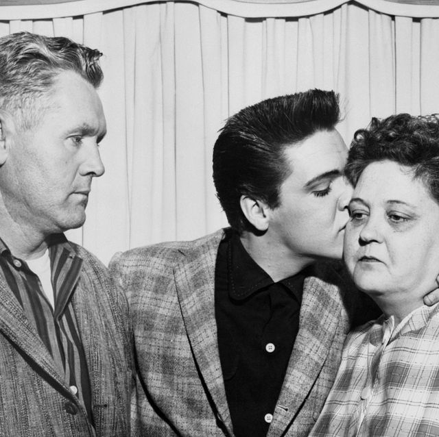 a black and white photo of elvis presley standing with his father and kissing his mother