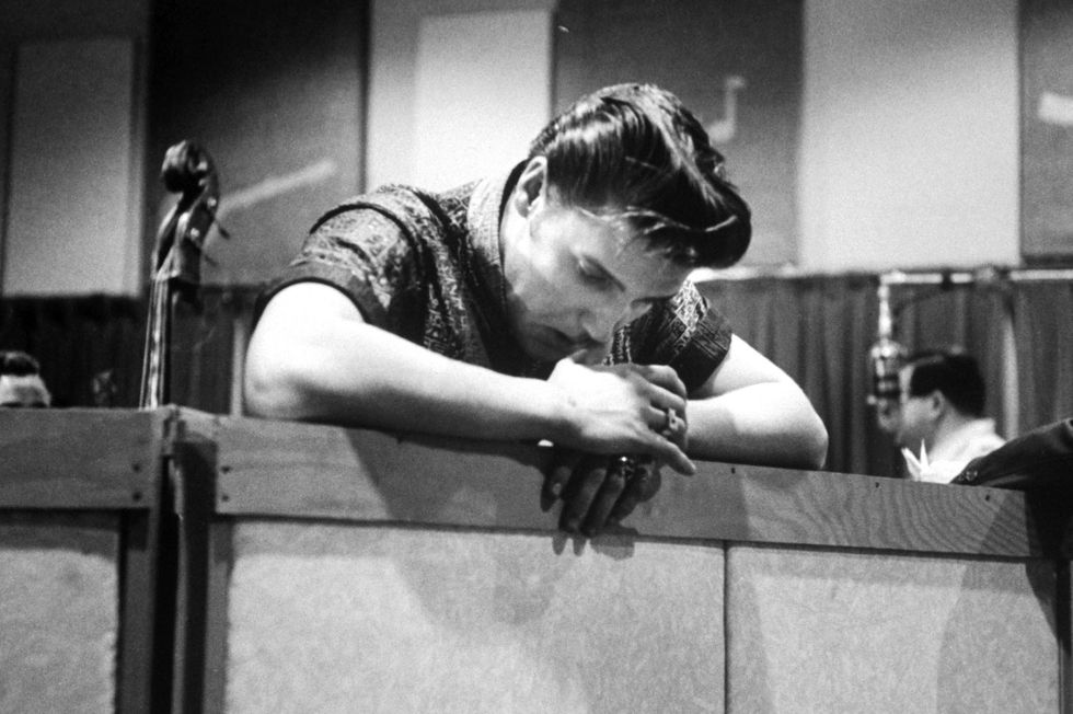 a black and white photo of elvis presley in a recording studio, resting his arms against a wall and looking down