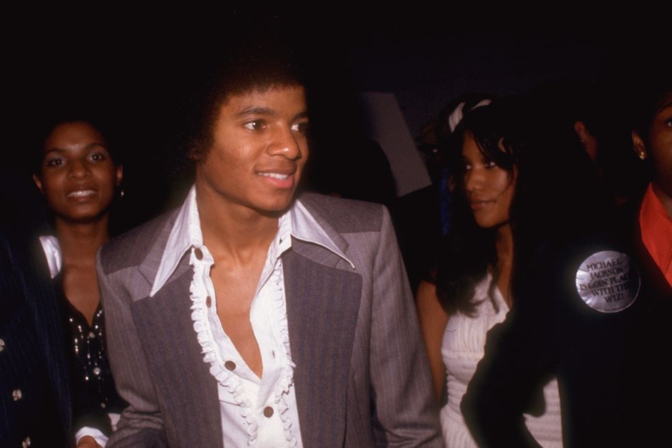 michael jackson wearing a purple suit and white shirt, looking off camera, with two women behind him
