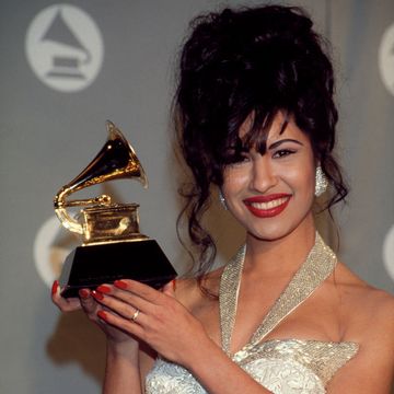selena quintanilla smiles at the camera and holds her grammy award, she wears a sparkling gown and large sparkling earrings