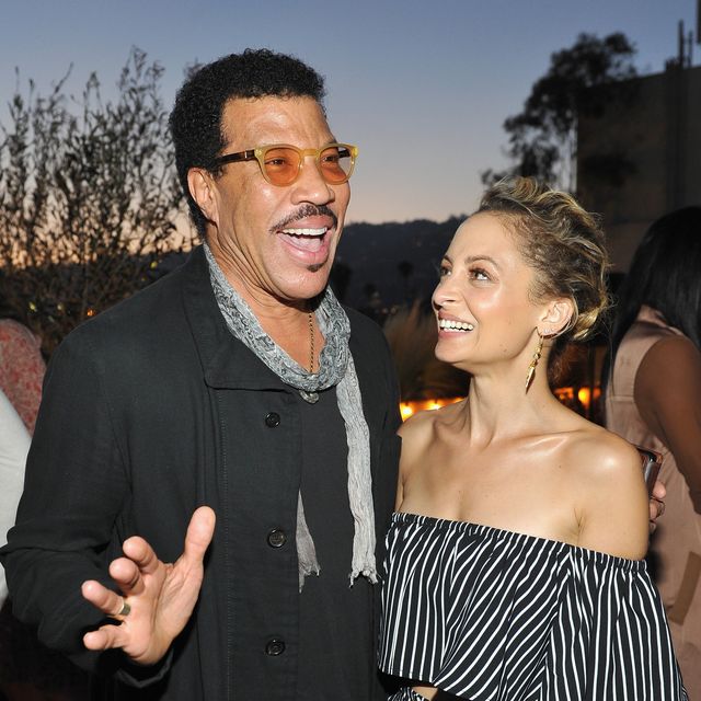 lionel richie and nicole richie stand together at an event, lionel is smiling as he speaks and has one arm around nicole who is looking at lionel and smiling