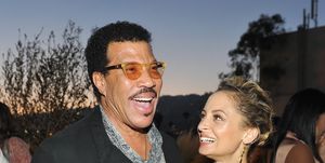 lionel richie and nicole richie stand together at an event, lionel is smiling as he speaks and has one arm around nicole who is looking at lionel and smiling