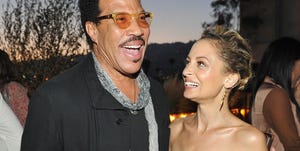 lionel richie and nicole richie stand together at an event, lionel is smiling as he speaks and has one arm around nicole who is looking at lionel and smiling