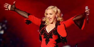 madonna wearing a black and red outfit while extending her arms and holding a microphone on a stage
